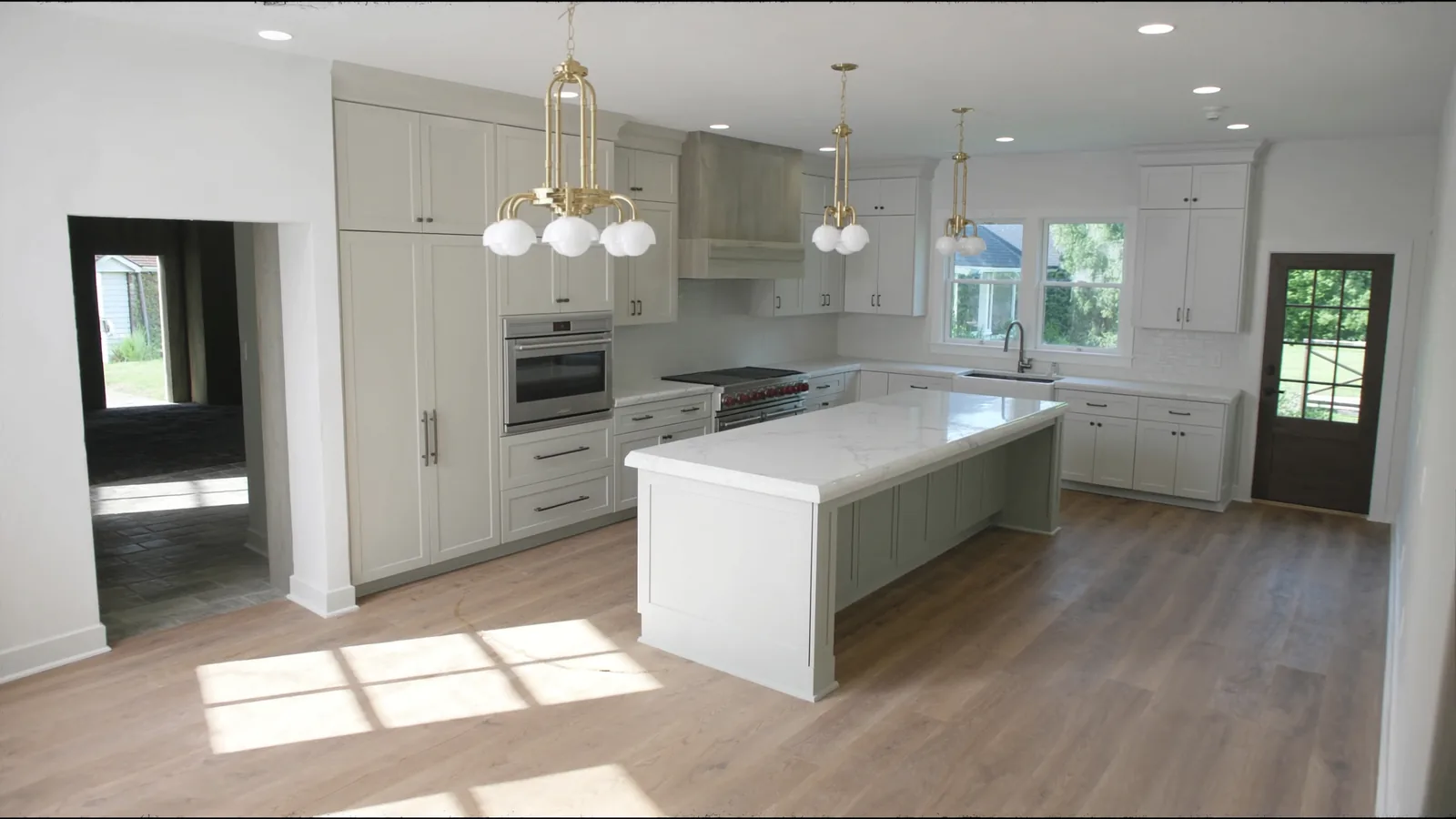 The same kitchen after remodel — bright white shaker cabinetry, oak island, quartz counters, brass hardware